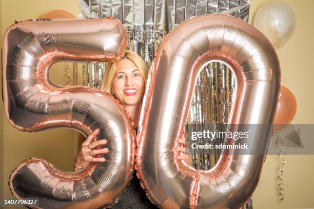 happy woman celebrating her 50th birthday with big age balloons - woman 50s blue eyes stock pictures, royalty-free photos & images