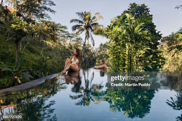 young couple relaxing on edge of luxury resort  infinity pool during a vacation, surrounded by tropical plants. - bali luxury stock pictures, royalty-free photos & images