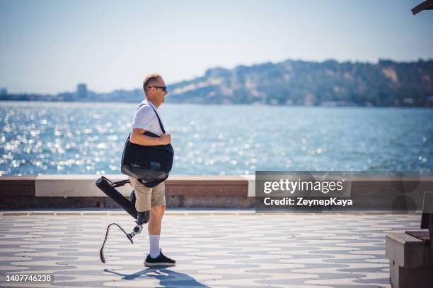 amputee man walking next to sea - artificial limb stockfoto's en -beelden