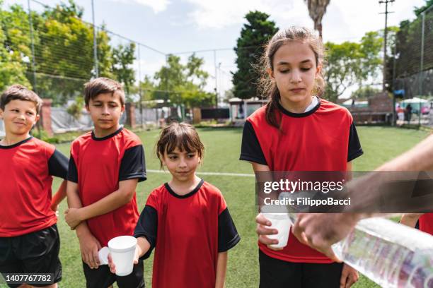coach filling a glass of water during a break on a soccer field. kids football team. males and females together. - girl filling water glass stock pictures, royalty-free photos & images