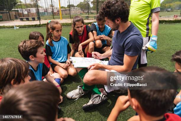 kids of a soccer team listening to their coach, sitting together on a soccer field - kids sports team stock pictures, royalty-free photos & images