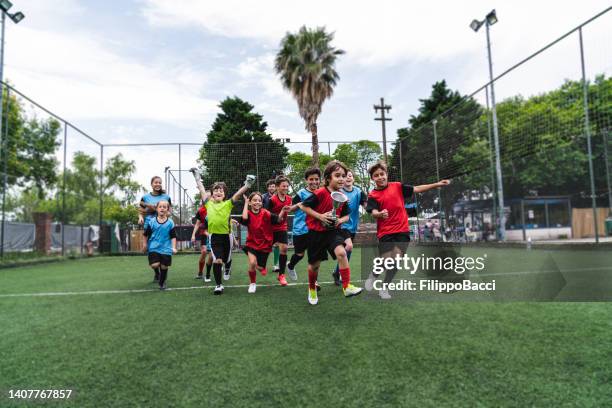 group of kids celebrating together the winning of a competition running on a soccer field - kids soccer team stock pictures, royalty-free photos & images