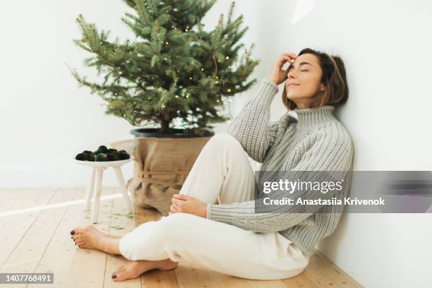 woman sitting near christmas tree at home. - womens month stock pictures, royalty-free photos & images