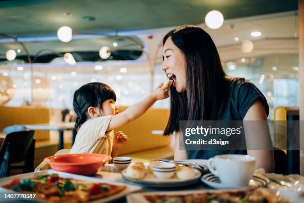 joyful young asian mother and lovely little daughter enjoying lunch together in restaurant. they are sharing food, enjoying family bonding time and a happy meal at the dining table. family and eating out lifestyle - parent and child meal stock pictures, royalty-free photos & images