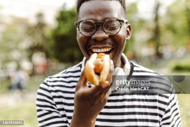 nahaufnahme porträt eines jungen mannes, der hot dog im freien isst - hot dog schnellimbiss stock-fotos und bilder