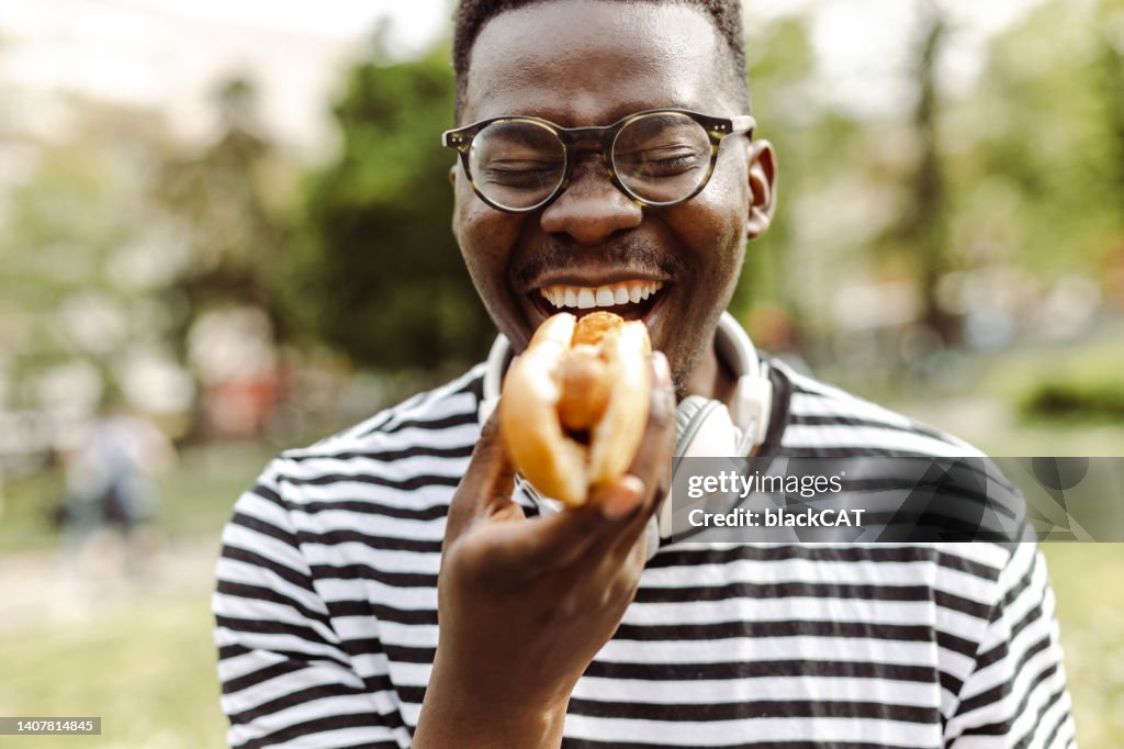 Close up portrait of young man eating hot dog outdoors