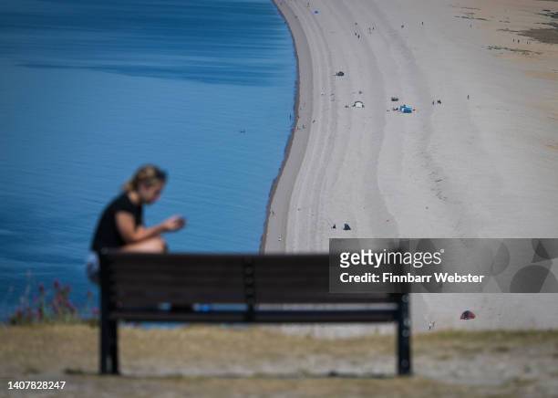 Person sits on the edge of a bench overlooking Chesil Beach, on July 10, 2022 in Portland, England. Britain will experience a heatwave this week as...