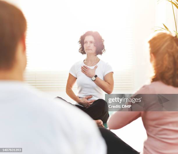 mature yoga instructor training people during a fitness class in a studio. yogi teaching breathing techniques with mindful meditating exercises for zen energy in lotus pose during a lesson indoors - peaceful demonstration stock pictures, royalty-free photos & images