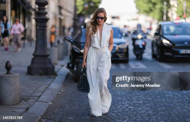 Ginta seen wearing back sunglasses from Yves Saint Laurent, diamond stud earrings, diamond necklace, a creme white linen suit vest and matching creme...