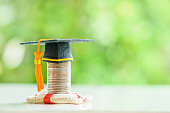 Tuition protection service and tuition refund insurance, financial concept : Black graduation cap or a mortarboard placed higher on top of a coin stack with a red lifebuoy on a table.