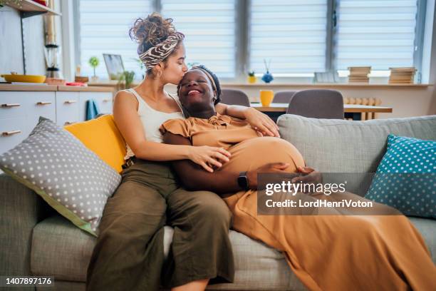 pregnant lesbian couple relaxing on sofa - black lesbians kiss stock pictures, royalty-free photos & images