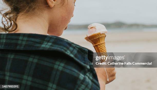 view of a little girl holding an ice-cream cone, looking over her shoulder - girl eating messy ice cream cone stock-fotos und bilder