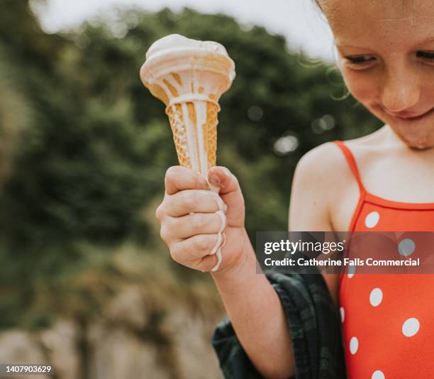 a little girl holds an ice-cream that is melting and dripping down her hand. - girl eating messy ice cream cone stock pictures, royalty-free photos & images