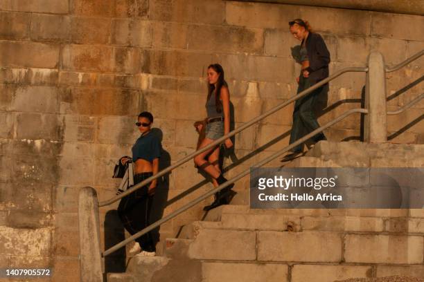 three beautiful confident young ladies, teenage girls walking down a sunbathed staircase at or around twilight judging by the golden light of the surroundings - southern european descent stock-fotos und bilder
