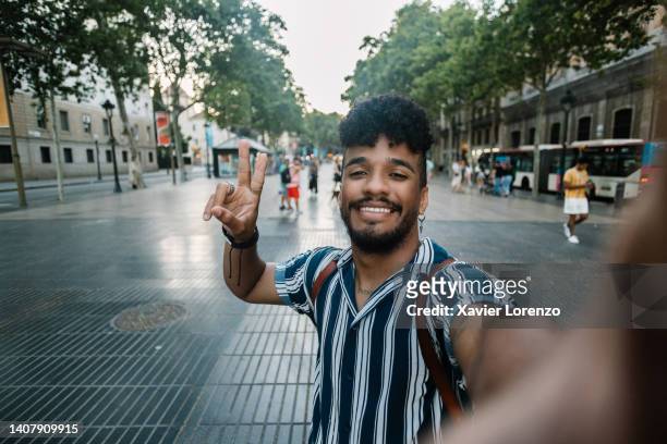 cheerful hispanic latino young man tourist taking self portrait in las ramblas while visiting barcelona on summer holidays - las ramblas fotografías e imágenes de stock