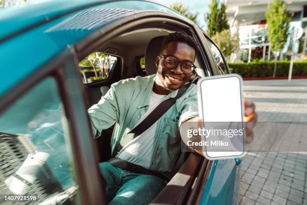 jeune homme assis dans la voiture et montrant un écran de téléphone intelligent - black car photos et images de collection