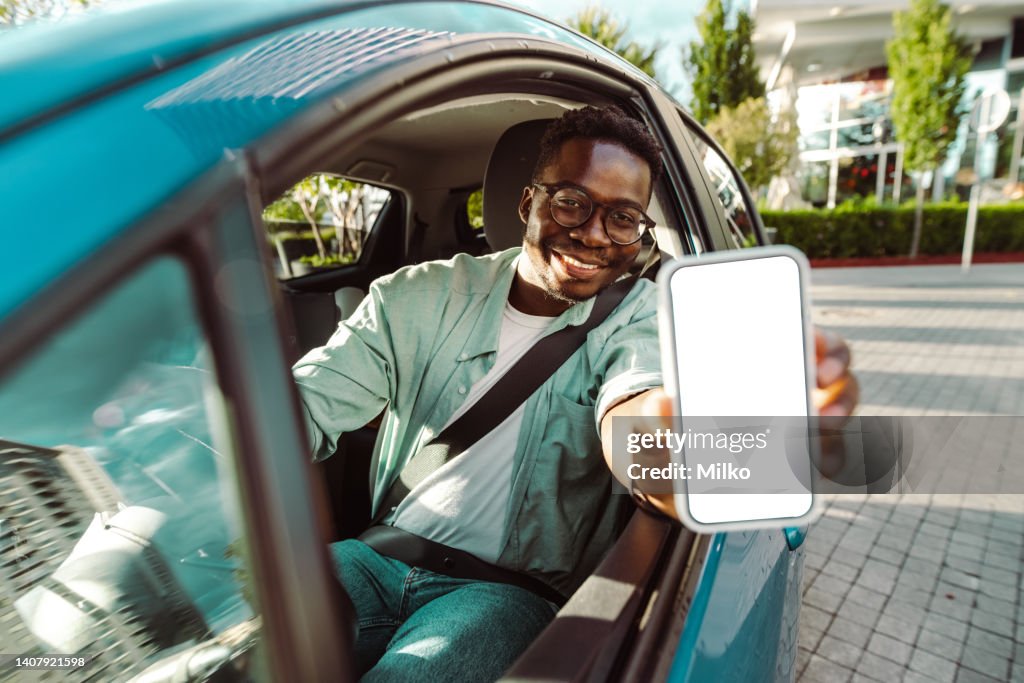 Young man sitting in the car and showing a screen of smart phone