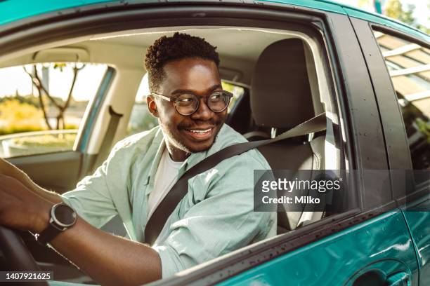 glücklicher afroamerikanischer männlicher fahrer, der ein auto fährt und durch das autofenster schaut - sicherheitsgurt stock-fotos und bilder