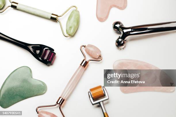 set of massage rollers for facial procedures on white background. metal, quartz, jade and dermarollers with microneedles. concept of dermatological treatment of different skin conditions. macro photography from above - massaggio del viso foto e immagini stock