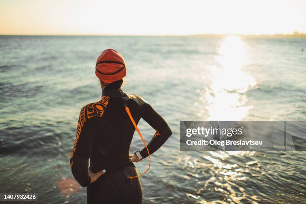 athlete ready to swim in open water at sunset. unrecognizable person from behind, triathlon training - open water swimming stock pictures, royalty-free photos & images