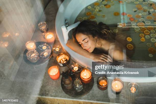 beautiful young woman relaxing in hot tub-bath with citrus oranges and lemons and with candles. - bath spa stock-fotos und bilder