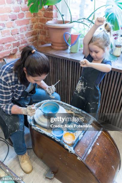 jeune maman et sa petite fille apprenant la poterie sur une roue de poterie, colorant le bol à moitié prêt avec la peinture de vitrage. - atelier enfant photos et images de collection