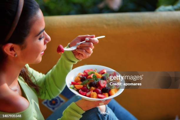 vegan food themes. close-up of a hispanic cute young woman eating fruit salad at lunch outdoors - eating fiber stock pictures, royalty-free photos & images