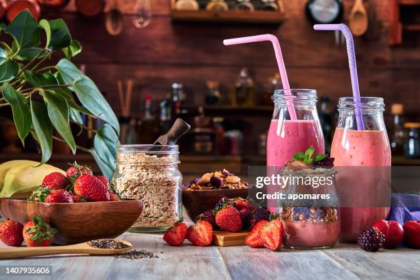 vegan food themes. set of three banana blackberry and strawberry smoothies with cereal in bottles with straws on a rustic table. - smoothies stock pictures, royalty-free photos & images