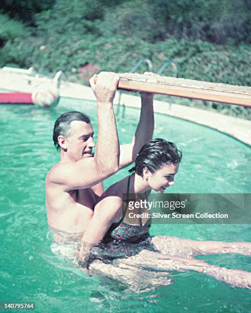 Stewart Granger , British actor, with his wife, Jean Simmons , British actress, in a swimming pool with Granger holding on to the diving board, circa...