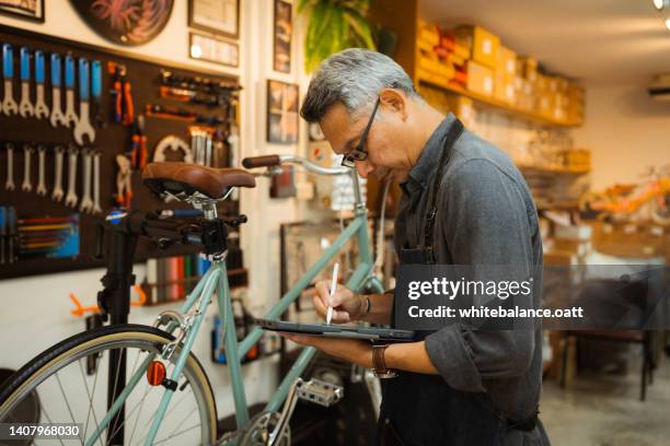 asian senior owner repairing bicycle. - bicycle shop 個照片及圖片檔