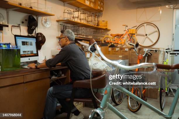 senior asian man working on laptop in bicycle shop. - bike shop stockfoto's en -beelden