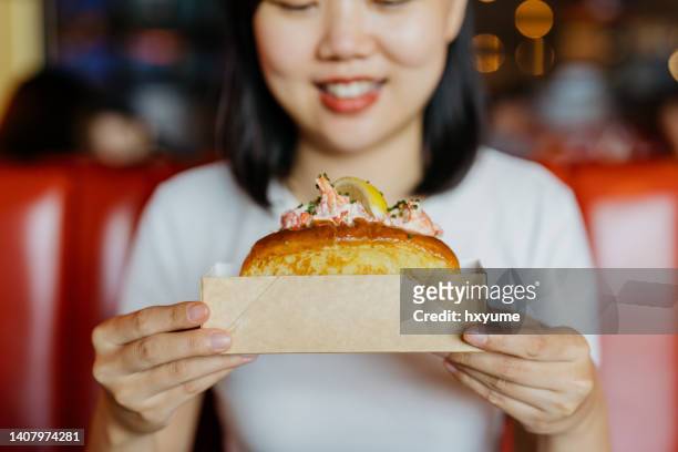 una mujer asiática sosteniendo un rollo de langosta en un recipiente de papel - langosta marisco fotografías e imágenes de stock