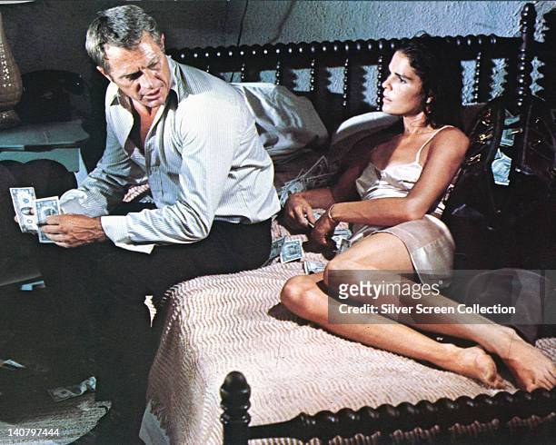 Steve McQueen , US actor, and Ali MacGraw, US actress, sitting on a bed counting banknotes in a publicity still issued for the film, 'The Getaway',...