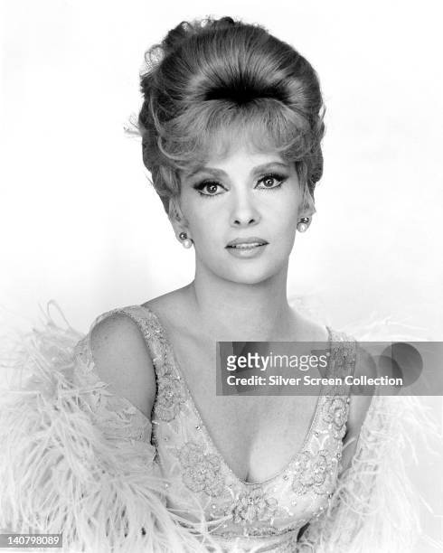 Gina Lollobrigida, Italian actress, wearing sequinned low-cut top, wrapped in a feather boa, in a studio portrait, against a white background, circa...