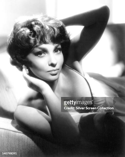 Gina Lollobrigida, Italian actress, wearing a low-cut thin strap white top in a studio portrait, with her hands up to her head, circa 1950.
