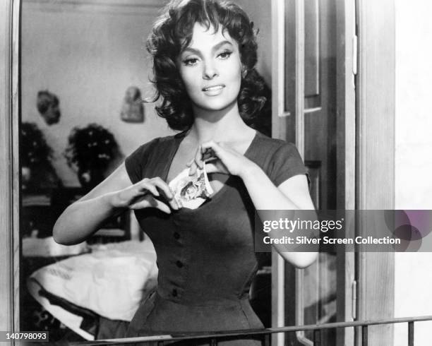 Gina Lollobrigida, Italian actress, putting a banknote down her cleavage in a publicity still issued for the film, 'The Law', Italy, 1956. Also...