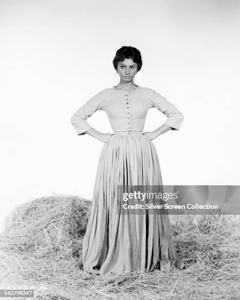 Sophia Loren, Italian actress, wearing a full-length dress, with a pleated skirt, with her hands on her hips, standing on straw, in a studio...