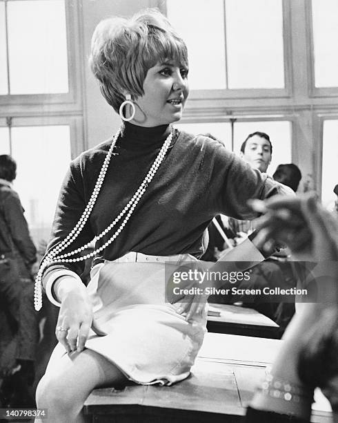 Lulu, British pop singer, dressed in sixties fashions, with a black jumper and a white miniskirt and a long pearl necklace and large hoop earrings,...
