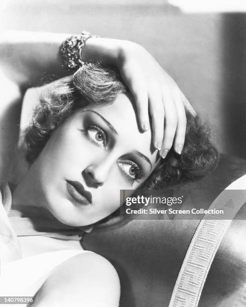 Headshot of Jeanette MacDonald , US singer and actress, posing with her left hand on her head, which rests against the backrest of a sofa in a studio...