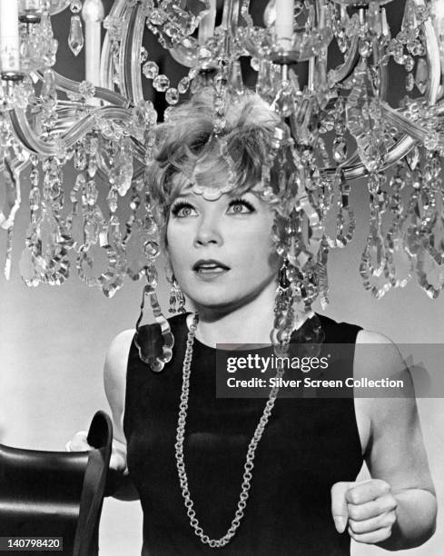 Shirley MacLaine, US actress, wearing a black sleeveless top with a long necklace, posing beneath a chandelier, circa 1965.