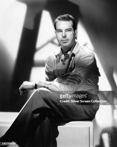 Fred MacMurray , US actor, sitting on a pedestal with his legs crossed, in a studio portrait, against background of shadows, circa 1950.