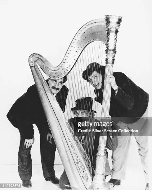 The Marx Brothers , US comedians, posing with a harp in a studio portrait, against a white background, circa 1935.