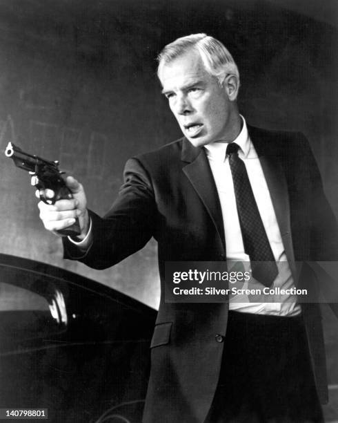 Lee Marvin , US actor, wearing a black suit with a white shirt and a black tie, brandishing a handgun, in an image issued as publicity for the film,...