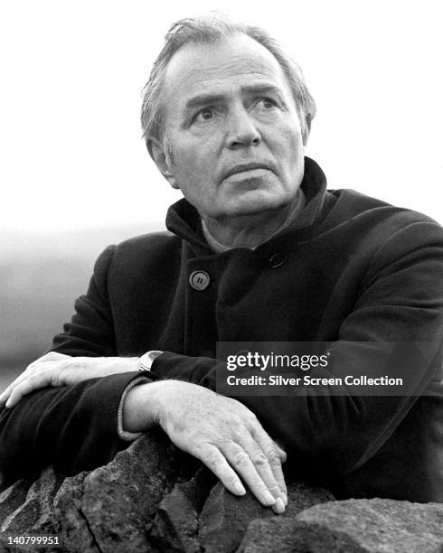 James Mason , British actor, wearing a black overcoat, leaning on a dry stone wall, circa 1970.