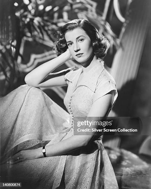 Lois Maxwell , Canadian actress, wearing a white button-front dress, posing with her elbow resting on her knee and her head resting against her hand,...