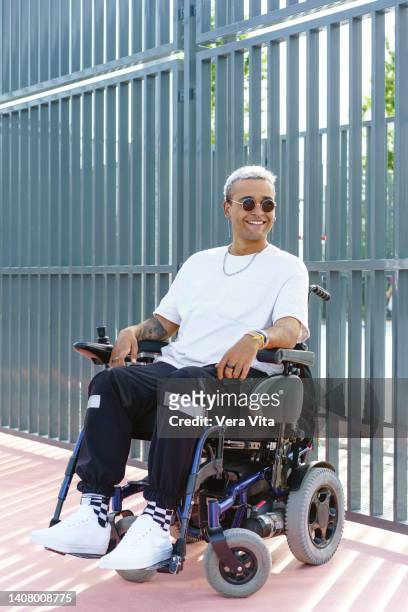vertical side view of disabled male with tattoos on wheelchair in urban clothes wearing sunglasses and white afro hair - man electric chair stock pictures, royalty-free photos & images
