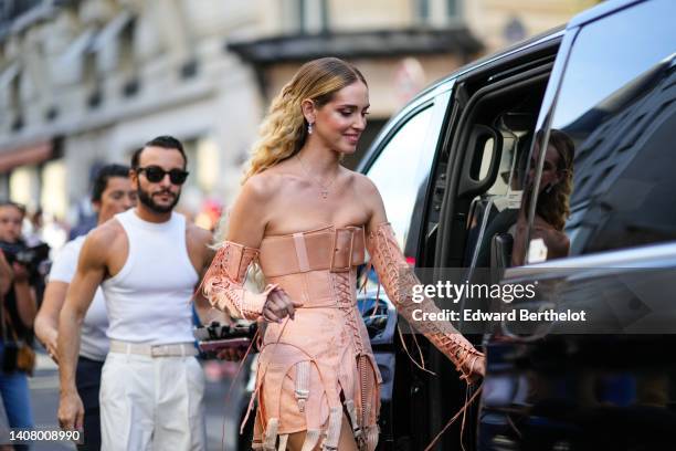 Chiara Ferragni wears silver and diamonds pendant earrings, a gold with cross pendant necklace, a beige shoulder-off / laces / corset short dress...