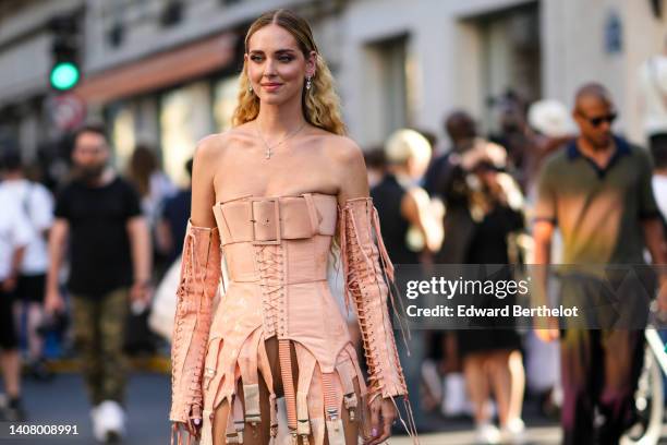 Chiara Ferragni wears silver and diamonds pendant earrings, a gold with cross pendant necklace, a beige shoulder-off / laces / corset short dress...