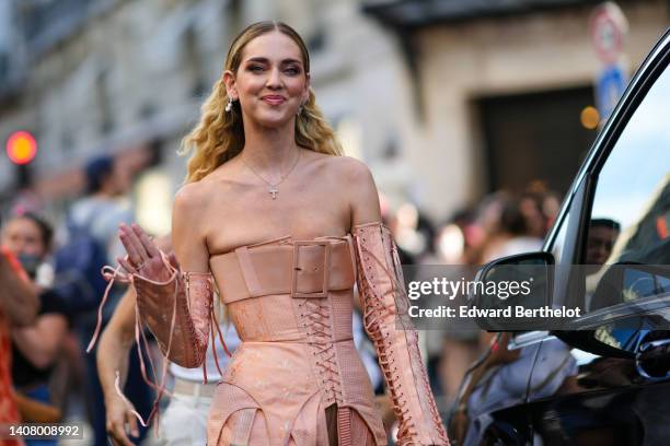 Chiara Ferragni wears silver and diamonds pendant earrings, a gold with cross pendant necklace, a beige shoulder-off / laces / corset short dress...