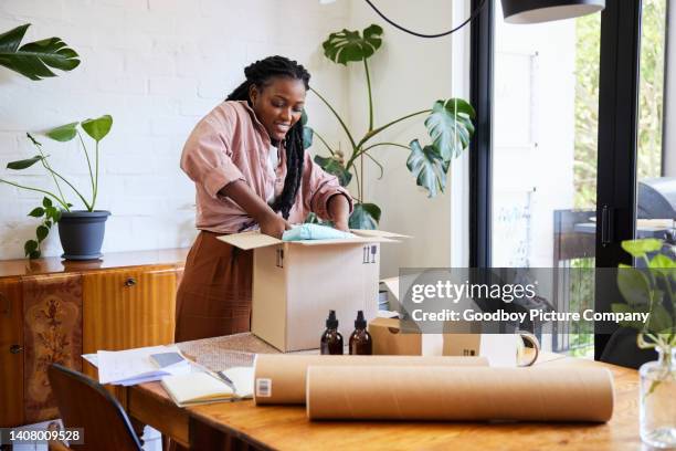 femme souriante qui emballe les commandes pour son entreprise à domicile à une table à manger - envelopper photos et images de collection
